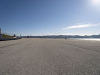 a person is skateboarding down a stretch of beach near a body of water with mountains in the distance