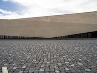 a street filled with cobblestones and concrete building with a sky in the background