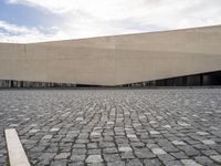 a street filled with cobblestones and concrete building with a sky in the background