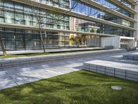 a picture of an office building near a sidewalk with benches and grass in front of it