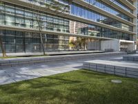 a picture of an office building near a sidewalk with benches and grass in front of it