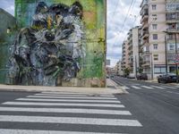 the mural is near two cars on the side of the road and buildings in the background