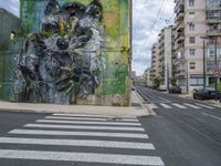 the mural is near two cars on the side of the road and buildings in the background