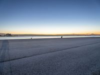 a lone person sitting on top of a bench at the beach by water at dusk