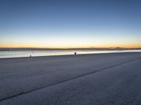 a lone person sitting on top of a bench at the beach by water at dusk