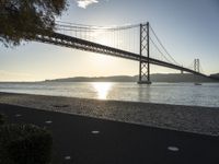 a view of a bridge across the ocean at sunset in a park with grass and shrubbery