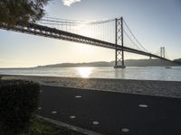 a view of a bridge across the ocean at sunset in a park with grass and shrubbery