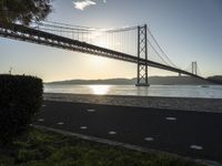 a view of a bridge across the ocean at sunset in a park with grass and shrubbery