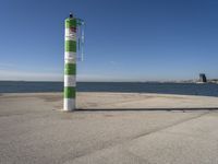 a green and white pole on a pier next to the water that reads beach road