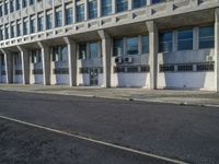 a tall building with concrete pillars in front of it that has closed doors with windows