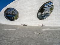 a modern building has two circular windows and two benches on the side of it,