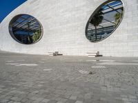 a modern building has two circular windows and two benches on the side of it,