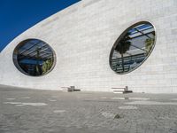 a modern building has two circular windows and two benches on the side of it,