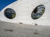 a modern building has two circular windows and two benches on the side of it,