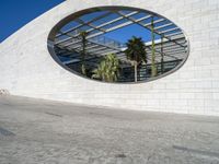 a circular mirror reflecting the blue sky in an outdoor courtyard area with stone and glass