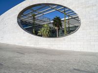 a circular mirror reflecting the blue sky in an outdoor courtyard area with stone and glass