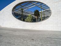 a circular mirror reflecting the blue sky in an outdoor courtyard area with stone and glass