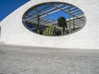 a circular mirror reflecting the blue sky in an outdoor courtyard area with stone and glass