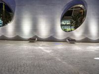 two benches sit on a tiled walkway in front of a building with circular windows above