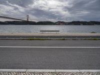 a bridge is above the ocean and some benches sit on the pavement in front of the water