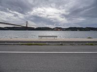 a bridge is above the ocean and some benches sit on the pavement in front of the water