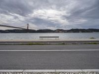 a bridge is above the ocean and some benches sit on the pavement in front of the water