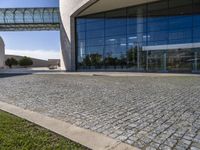 brick pathway in front of building, with lawn and walkway and open entry doors, with large windows, glass walls and steel arch