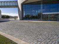 brick pathway in front of building, with lawn and walkway and open entry doors, with large windows, glass walls and steel arch