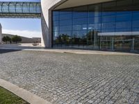 brick pathway in front of building, with lawn and walkway and open entry doors, with large windows, glass walls and steel arch