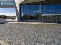 brick pathway in front of building, with lawn and walkway and open entry doors, with large windows, glass walls and steel arch