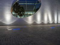 a large building with a circular mirror at night, with the surrounding concretes, has blue lighting from outside