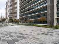 the empty street has grey bricked sidewalks in front of tall buildings and a fenced area