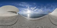 a fisheye lens image showing an ocean view with a large circular structure on one corner and a building on the other