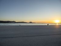 an empty street on top of a beach with the sun rising in front of a couple