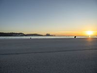 an empty street on top of a beach with the sun rising in front of a couple