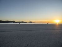 an empty street on top of a beach with the sun rising in front of a couple