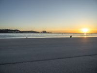 an empty street on top of a beach with the sun rising in front of a couple