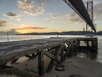 the sun sets over the water on a beach as the bridge crosses the ocean in the distance