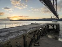 the sun sets over the water on a beach as the bridge crosses the ocean in the distance