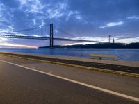 car drives along an empty road by the water and bridge on a cloudy day in the distance