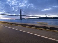 car drives along an empty road by the water and bridge on a cloudy day in the distance