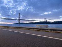 car drives along an empty road by the water and bridge on a cloudy day in the distance