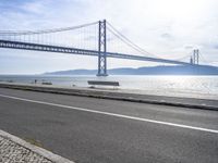 a car driving past a suspension bridge over the water next to the ocean on a sunny day