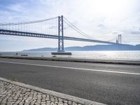 a car driving past a suspension bridge over the water next to the ocean on a sunny day