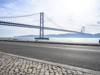 a car driving past a suspension bridge over the water next to the ocean on a sunny day