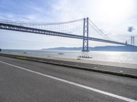 a bike rider rides past a bridge spanning the ocean with mountains behind him in a blue sky