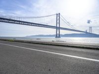 a bike rider rides past a bridge spanning the ocean with mountains behind him in a blue sky