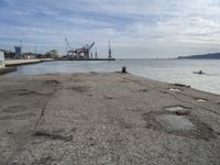 a concrete pier on the edge of the water in a city with cranes in the distance