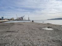 a concrete pier on the edge of the water in a city with cranes in the distance