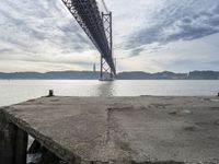 an empty pier at a bridge and water underneath it in the foreground and blue sky